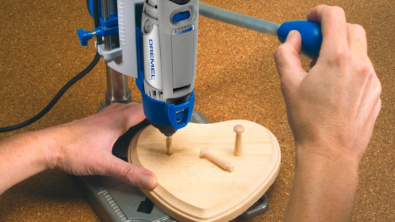 A person using a workstation drill press attachment for a rotary tool
