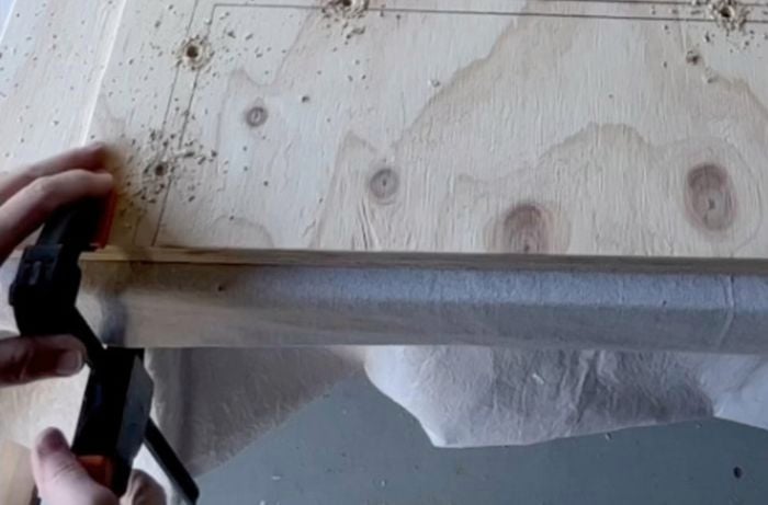 Holes pre drilled into a piece of plywood spaced in a line, evenly apart.