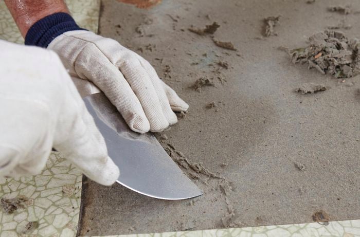 Gloved person scraping paper backing off the floor