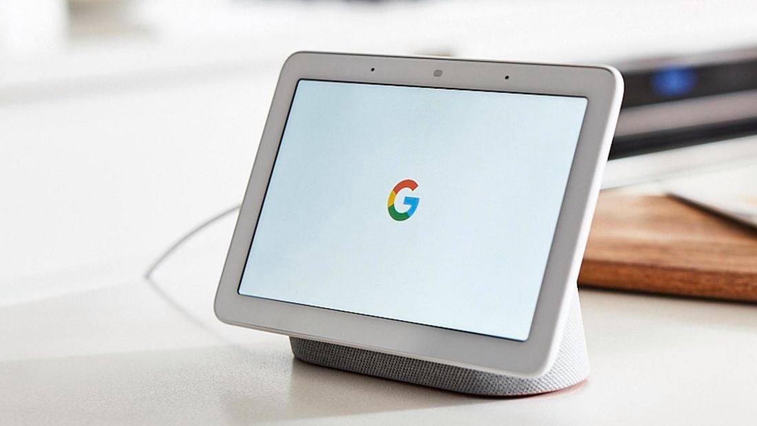 A google tablet sitting in a charger in front of a chopping board in a white themed kitchen