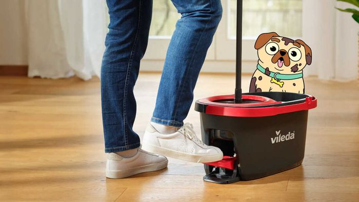 A person using a Vileda mop bucket on floorboards with an animated dog in the background.
