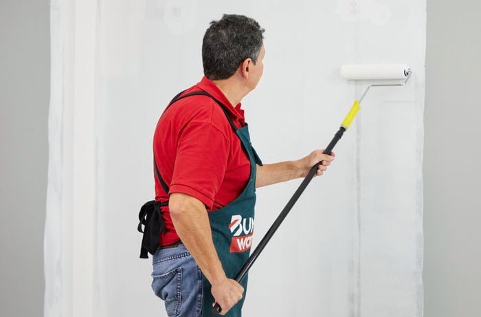 A man uses a paint roller to apply an undercoat to an interior wall.
