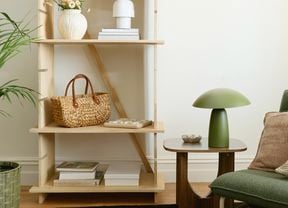 A light-coloured wooden display unit with adjustable shelves, holding decorative items, next to a potted plant.
