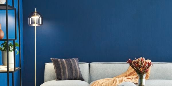 Living room with vibrant blue walls, a wooden coffee table and grey couch behind it, next to a gold floor lamp.