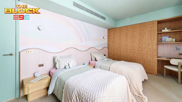 Contemporary twin bedroom featuring pastel bedding, a curved pink feature wall, timber wardrobes and a built-in study desk.