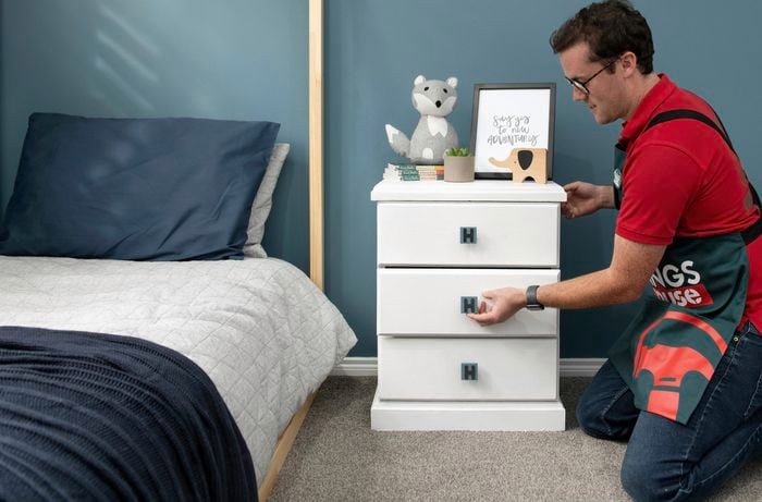 A white chest of drawers with handles customised with the letter H, in a blue themed bedroom setting