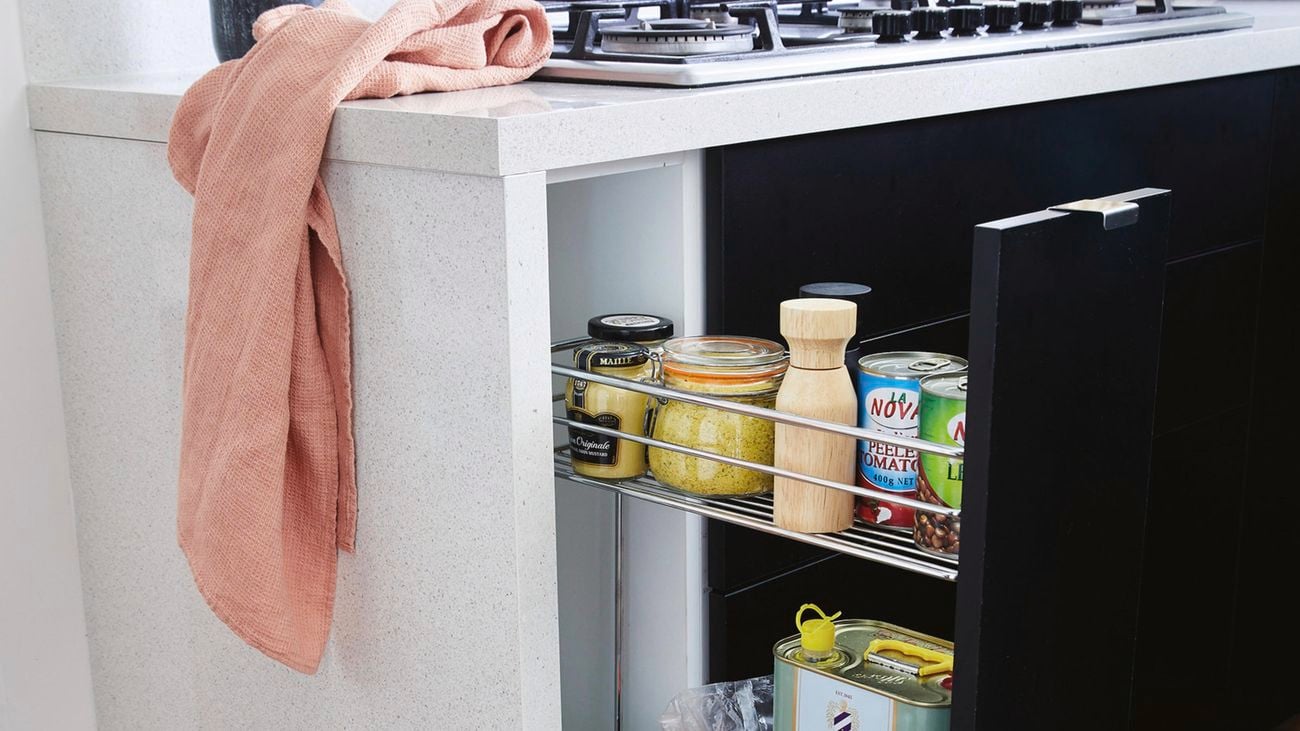 Pull-out wire basket in a narrow black cabinet.