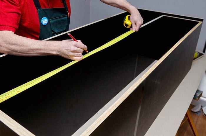 Person measuring and marking divider positions in cabinet