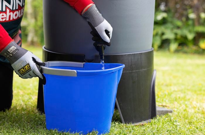 Bunnings employee turns on rainwater tank tap and water runs into a blue bucket.
