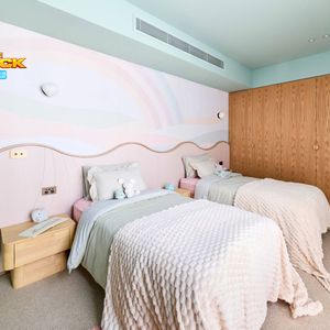 Contemporary twin bedroom featuring pastel bedding, a curved pink feature wall, timber wardrobes and a built-in study desk.