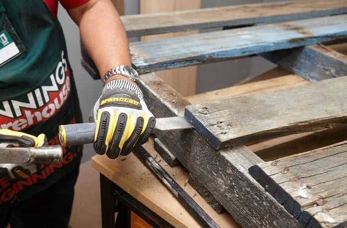 A person using a hammer and chisel to remove a slat from a pallet