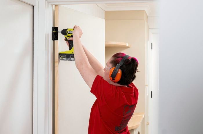 ​A ​​Bunnings​​ Team Member is securing the door hinges with remaining screws after testing door movement and confirming correct alignment.