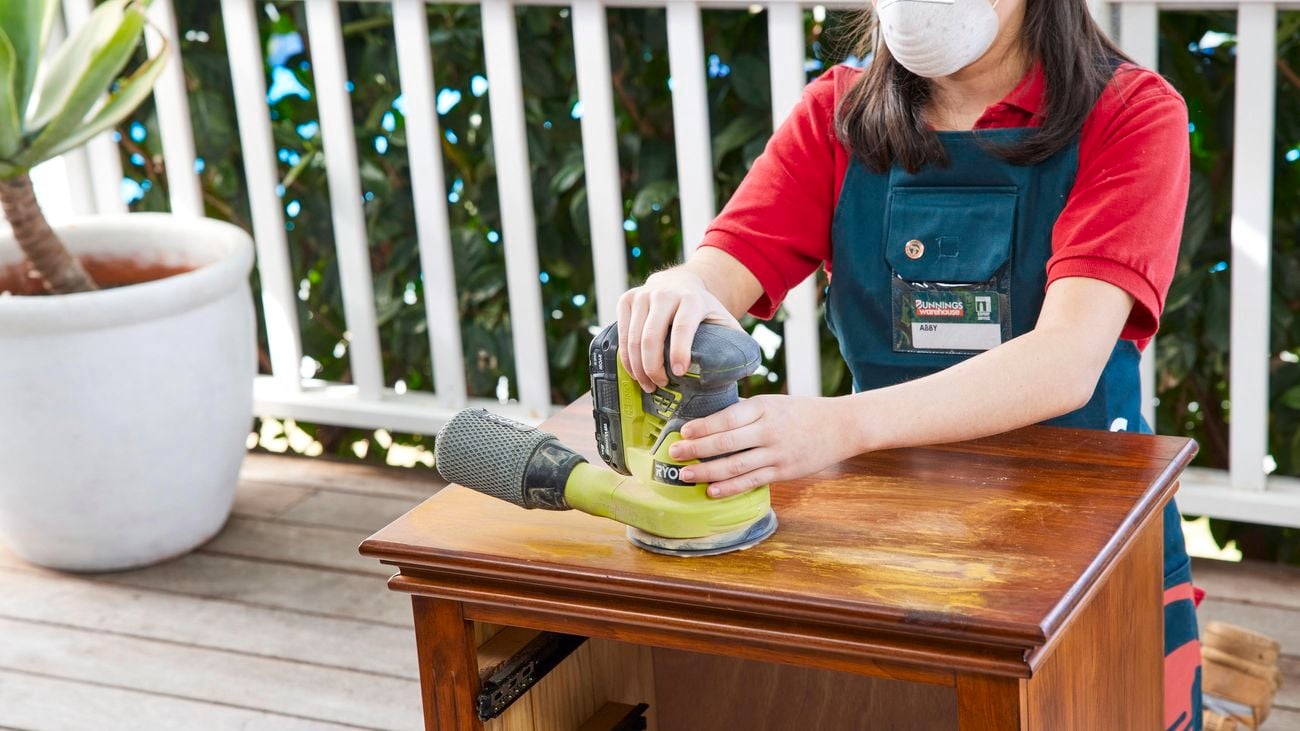 Person using an orbital sander to sand the top of the bedside table.