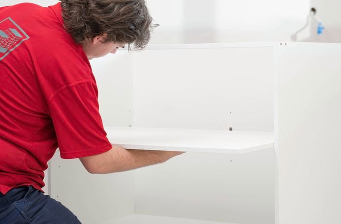 A Bunnings Team Member is installing a shelf inside the cabinet.