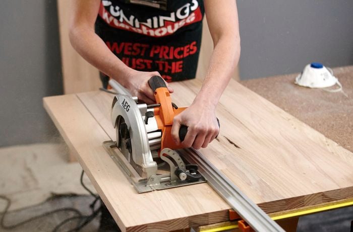A person cutting a timber panel using a circular saw and straight edge