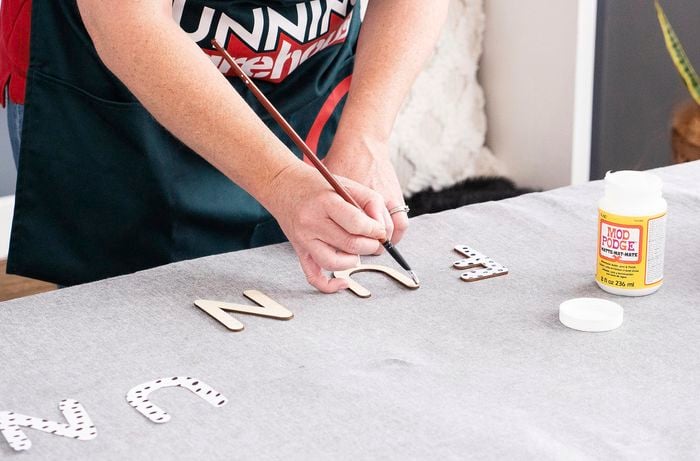 Person painting glue onto wooden letter.