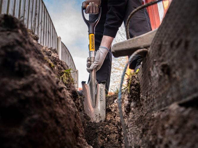 Roughneck Micro Drainage Shovel digging a trench in soil.