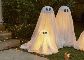 Halloween ghost decorations in a garden at night, surrounded by fairy lights.