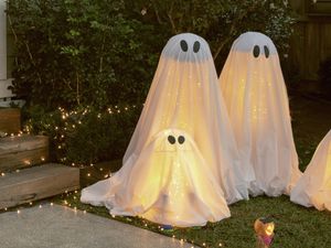 Halloween ghost decorations in a garden at night, surrounded by fairy lights.