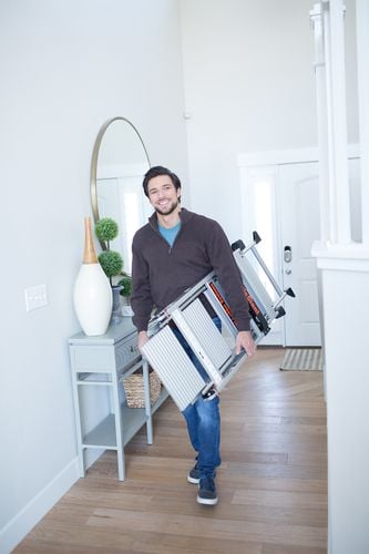 Person carrying ladder under their arm in home