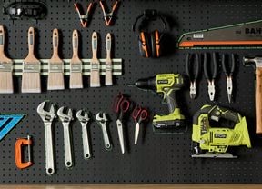 A pegboard displaying a variety of hand and power tools, including paint brushes, wrenches, pliers, a saw, a drill, and a jigsaw.