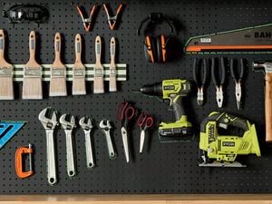 A pegboard displaying a variety of hand and power tools, including paint brushes, wrenches, pliers, a saw, a drill, and a jigsaw.
