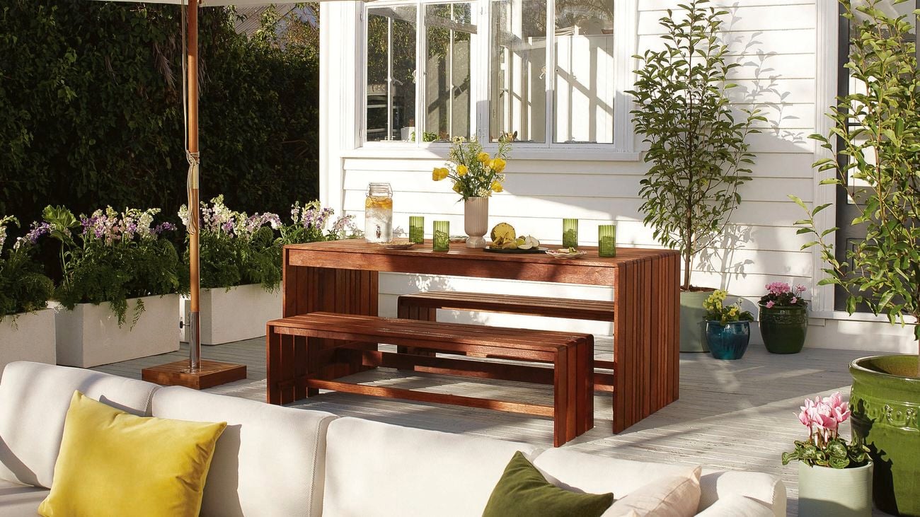An outdoor area is decked out with wooden tables and chairs and white sun umbrella