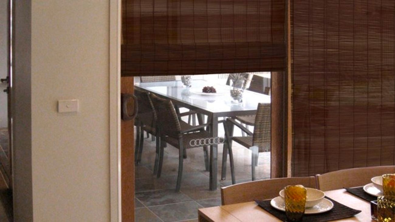 Brown matchstick blinds covering a glass sliding door to an outdoor area.