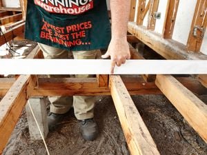 Person running a straight edge over floor joists, pointing to gap