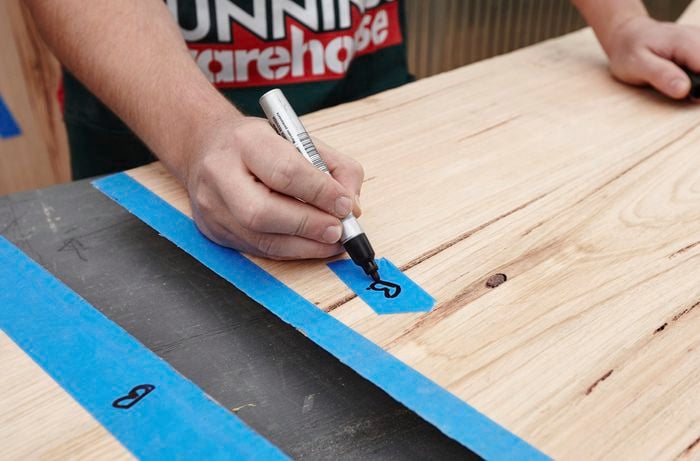 A person writing the letter B on a piece of masking tape on a length of timber