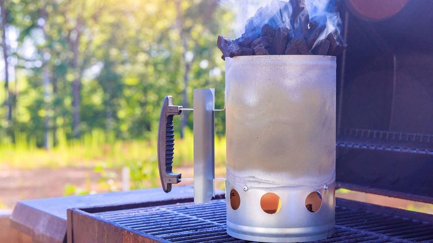 Chimney starter full of charcoal with lit Firestarters beneath, sitting on BBQ grill
