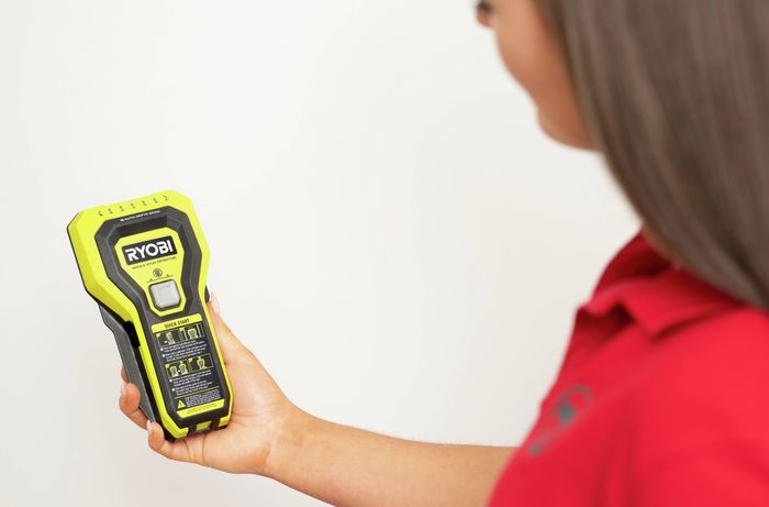 Person holding a yellow stud finder and viewing the display before use.