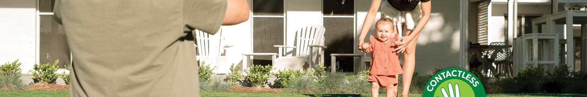 Man in foreground taking photo of his wife and toddler-aged daughter playing in backyard