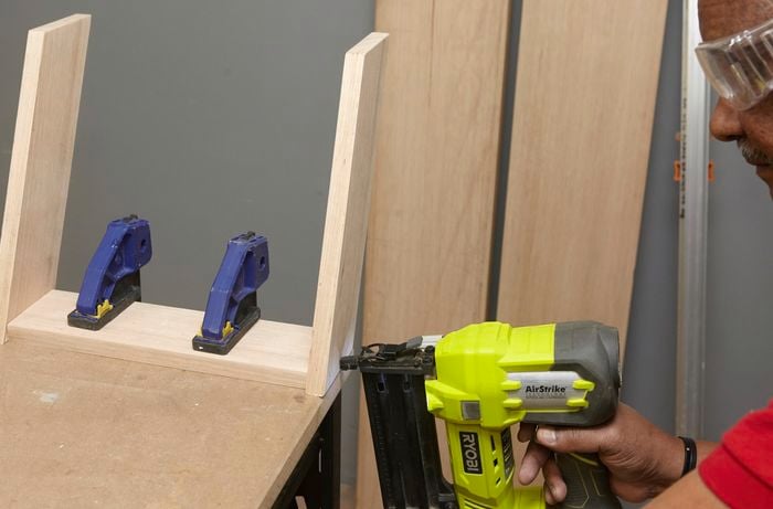 Person using nail gun to secure two pieces of timber together to form the folding back leg of DIY wooden step stool.