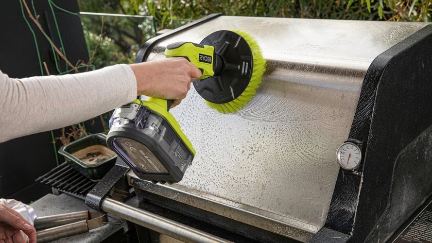 A person using a scrubber to clean a BBQ machine, with soapy water and suds visible on the surface.