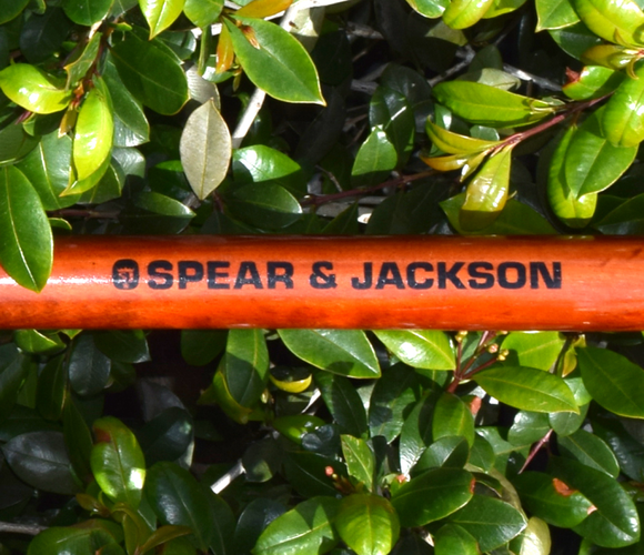 Close up of tool handle with brand label "Spear and Jackson" on a background of leaves