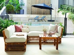 Outdoor lounge in the foreground with a pool, umbrella and sunlounges in the background.
