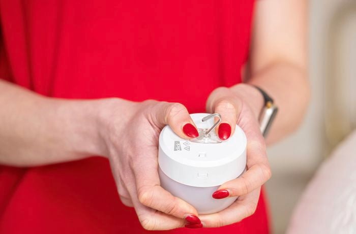 Person holding a rechargeable bulb with a hook before installing it into a pendant shade.