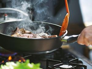 Close up of a hot pan cooking steak on a high heat.