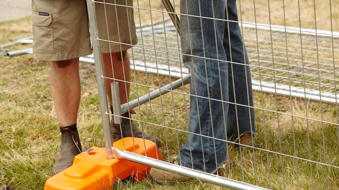 Two people positioning a safety strut into a concrete block holding temporary fencing