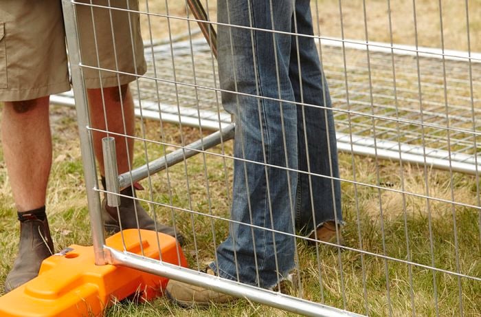 Two people positioning a safety strut into a concrete block holding temporary fencing