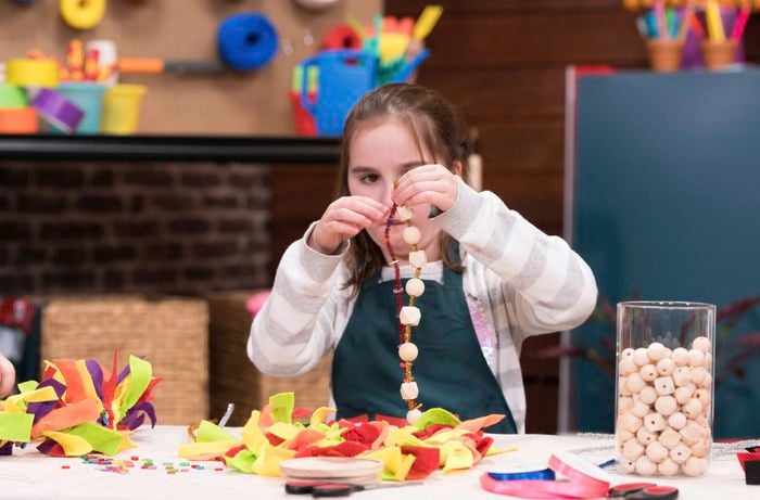 A young girl is stringing beads and ribbon bows on the table