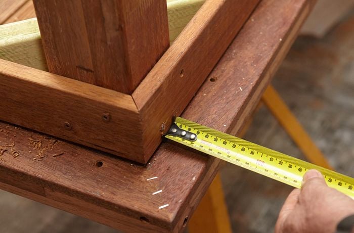 Person measuring the end of a table that is upside down.