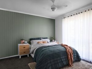 Bedroom with green panelled wall and bed with a blue cover next to a large window with sheer curtains