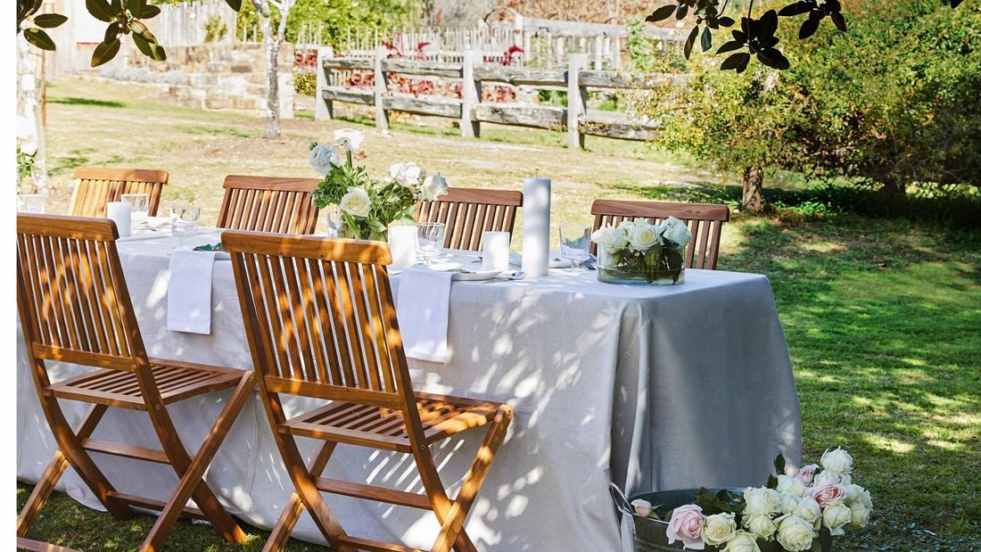 An outdoor table set with a white tablecloth, flowers and napkins.