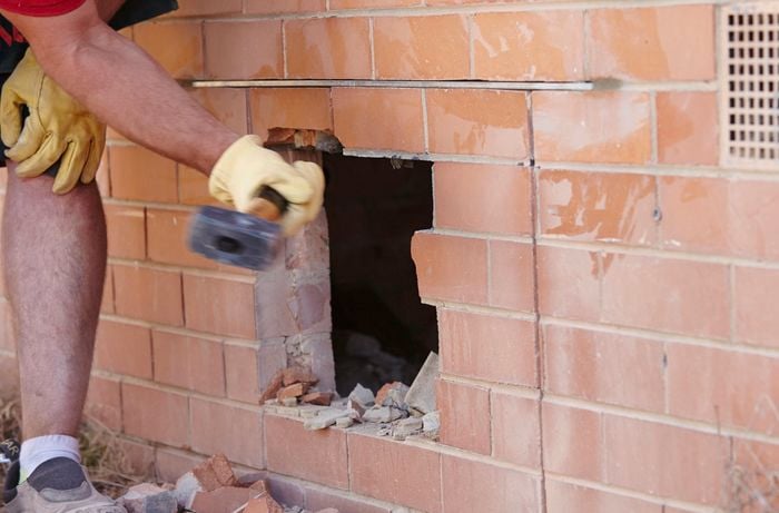 A mash hammer being used to knock bricks out of an opening in the wall