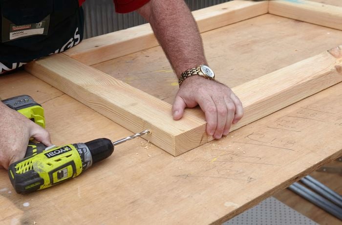 A person drilling a hole in pine timber