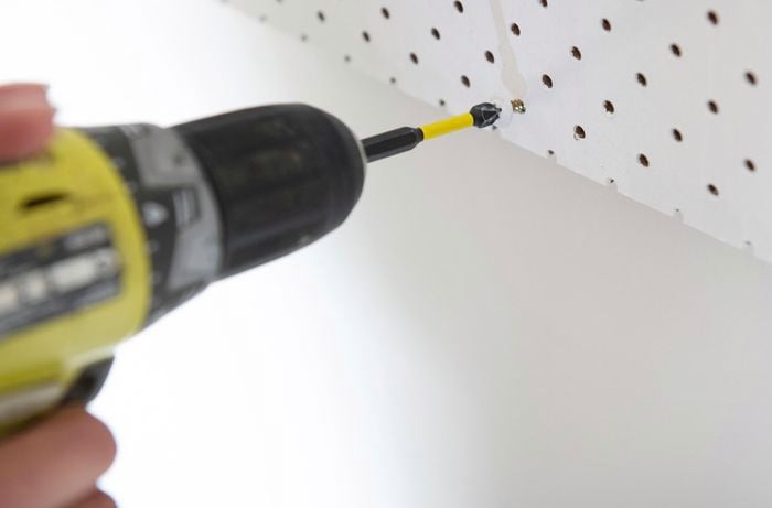 Screw being drilled into pegboard wall hole.