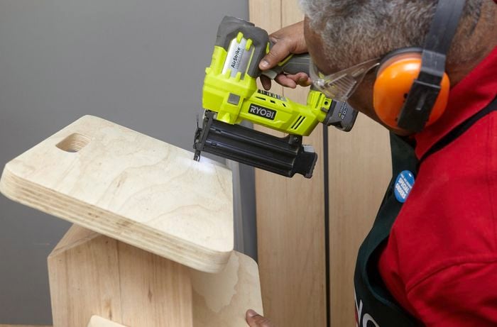 Person using nail gain to firmly secure top step of DIY wooden step stool.