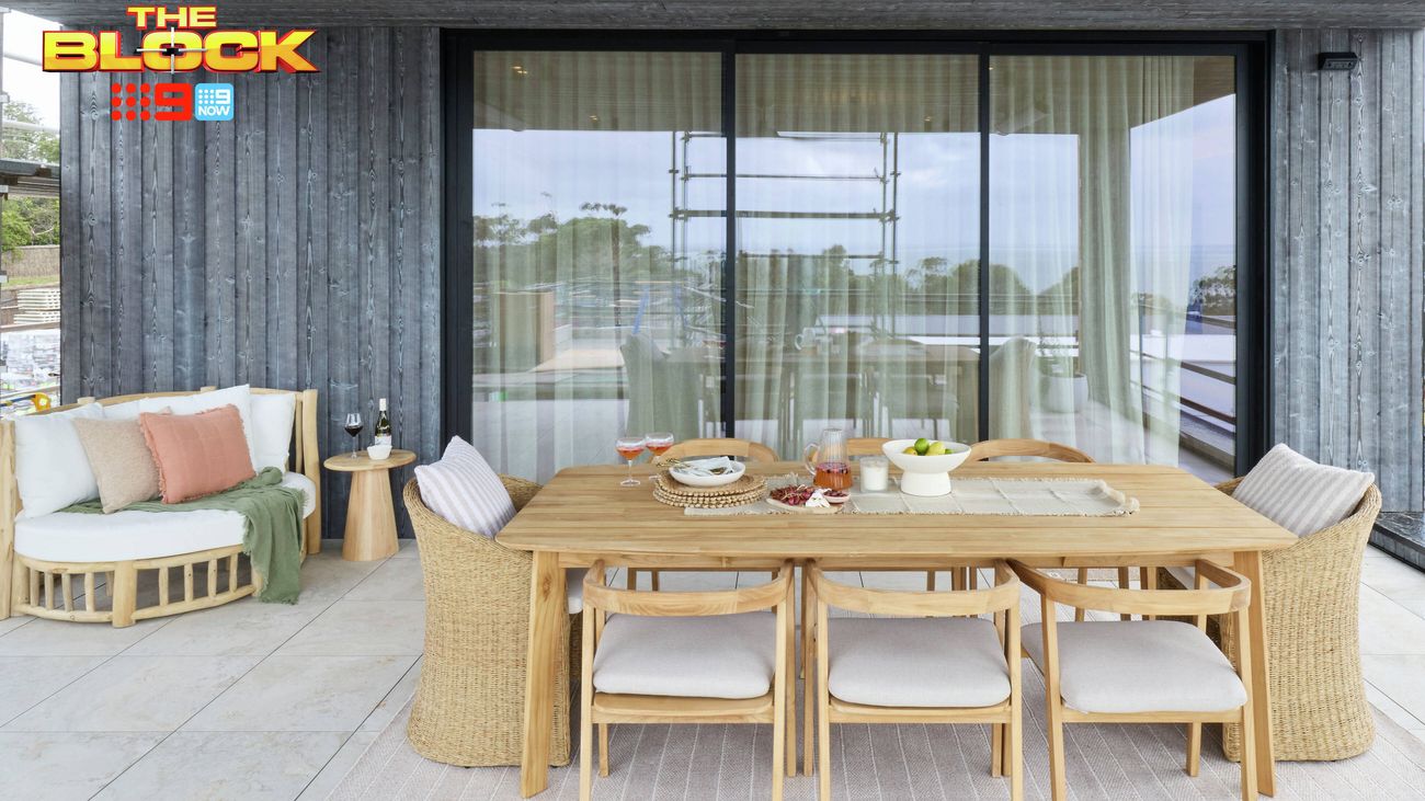 Outdoor dining area featuring a timber table and chairs, styled seating and large glass doors overlooking the landscape.